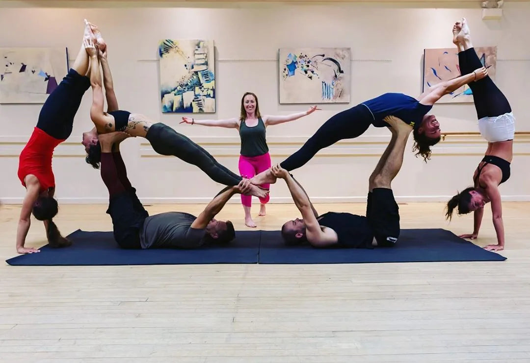 A group doing partner acrobatic yoga together on one long navy mat in a studio