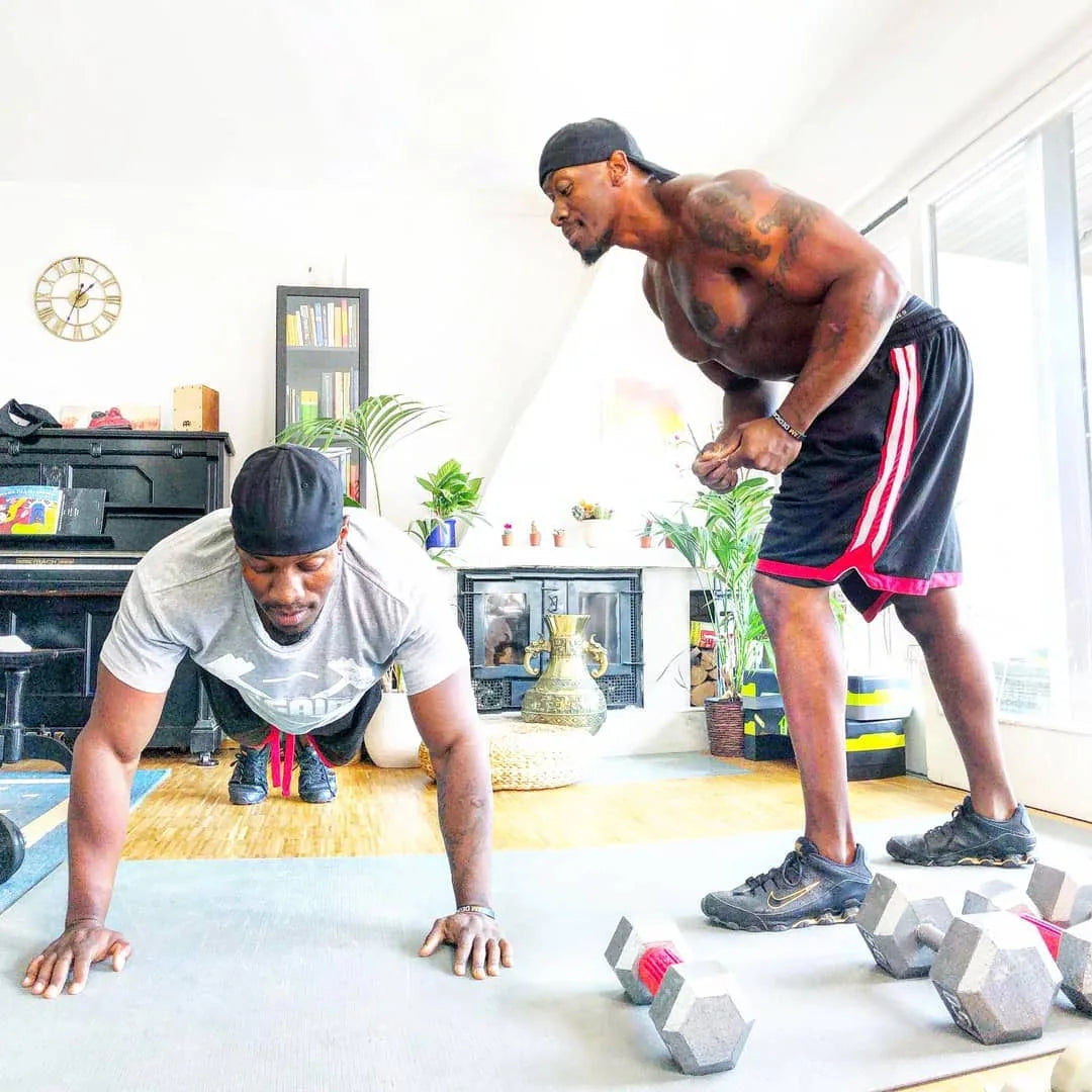 Two men training together on a large mat in a sunny living room