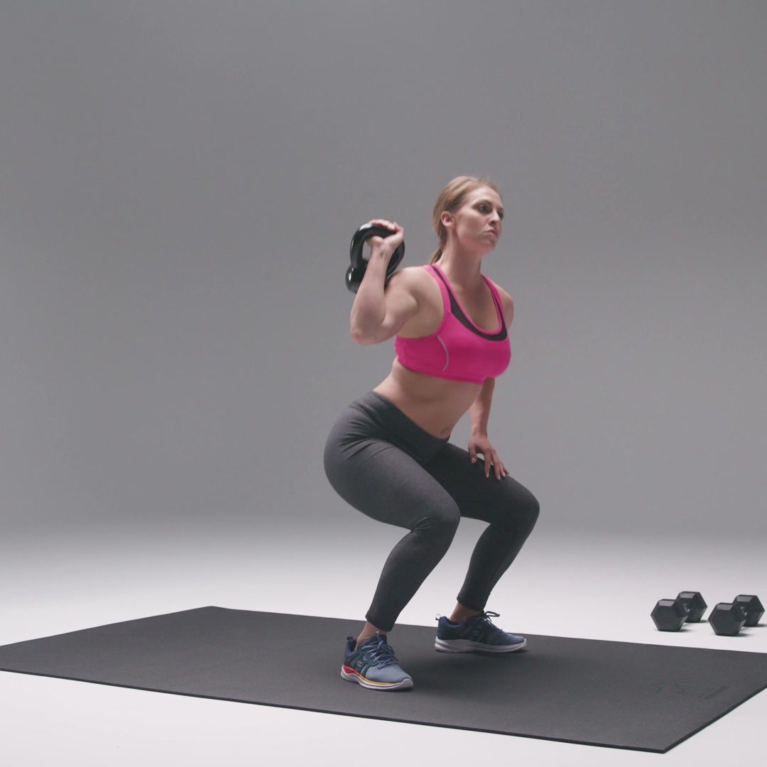 Woman in sneakers doing a kettlebell squat on a large black exercise mat