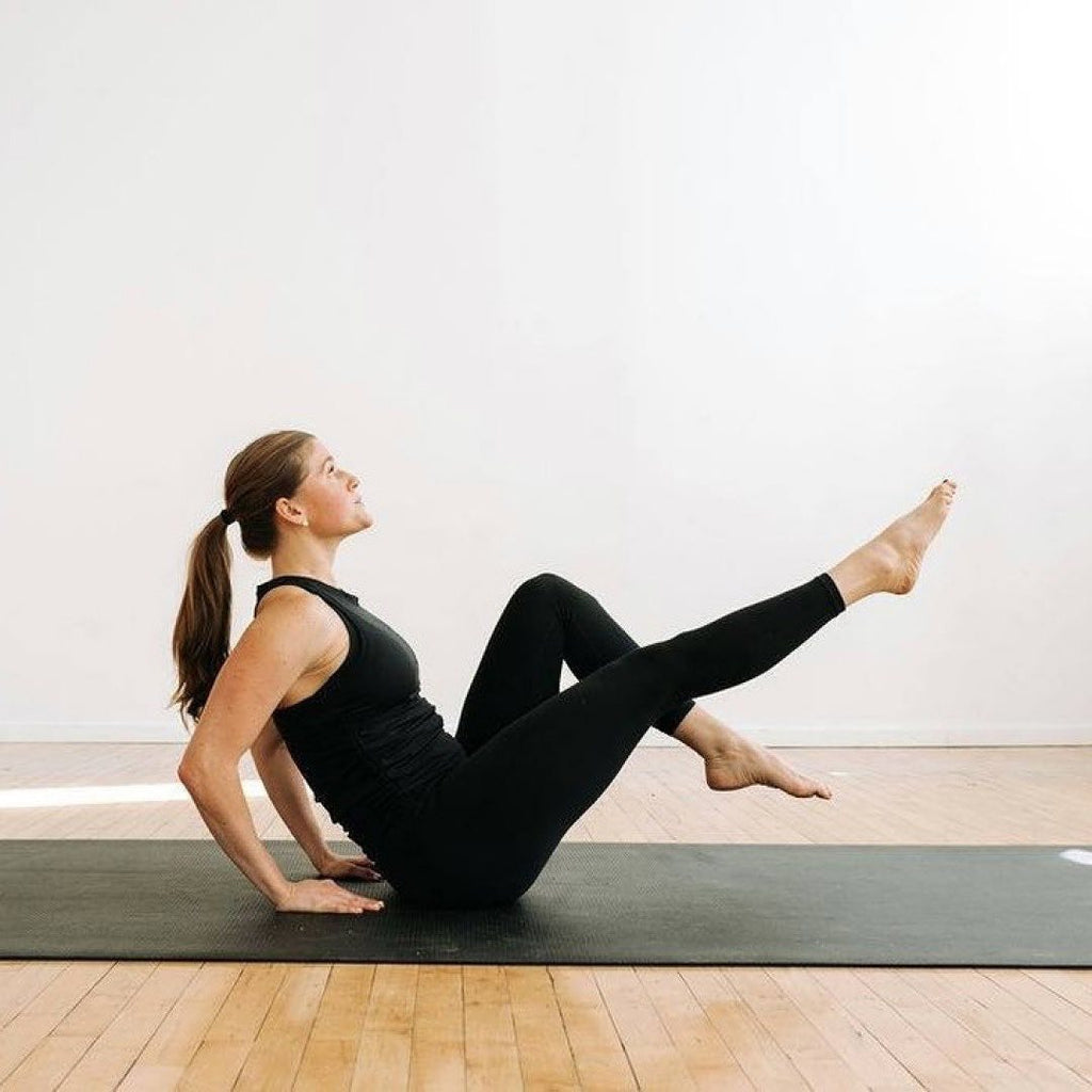 Woman in a seated pilates leg lift on a large black yoga mat