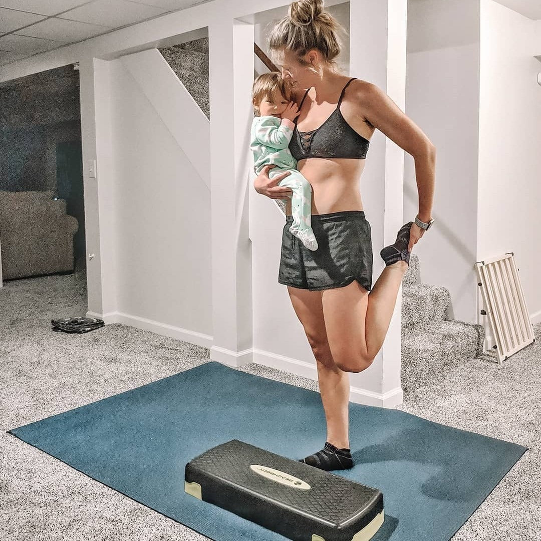 Woman in a standing quad stretch holding her baby on a large Oasis Blue yoga mat