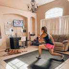 Woman in sneakers doing a deep lunge on a large black exercise mat in her living room