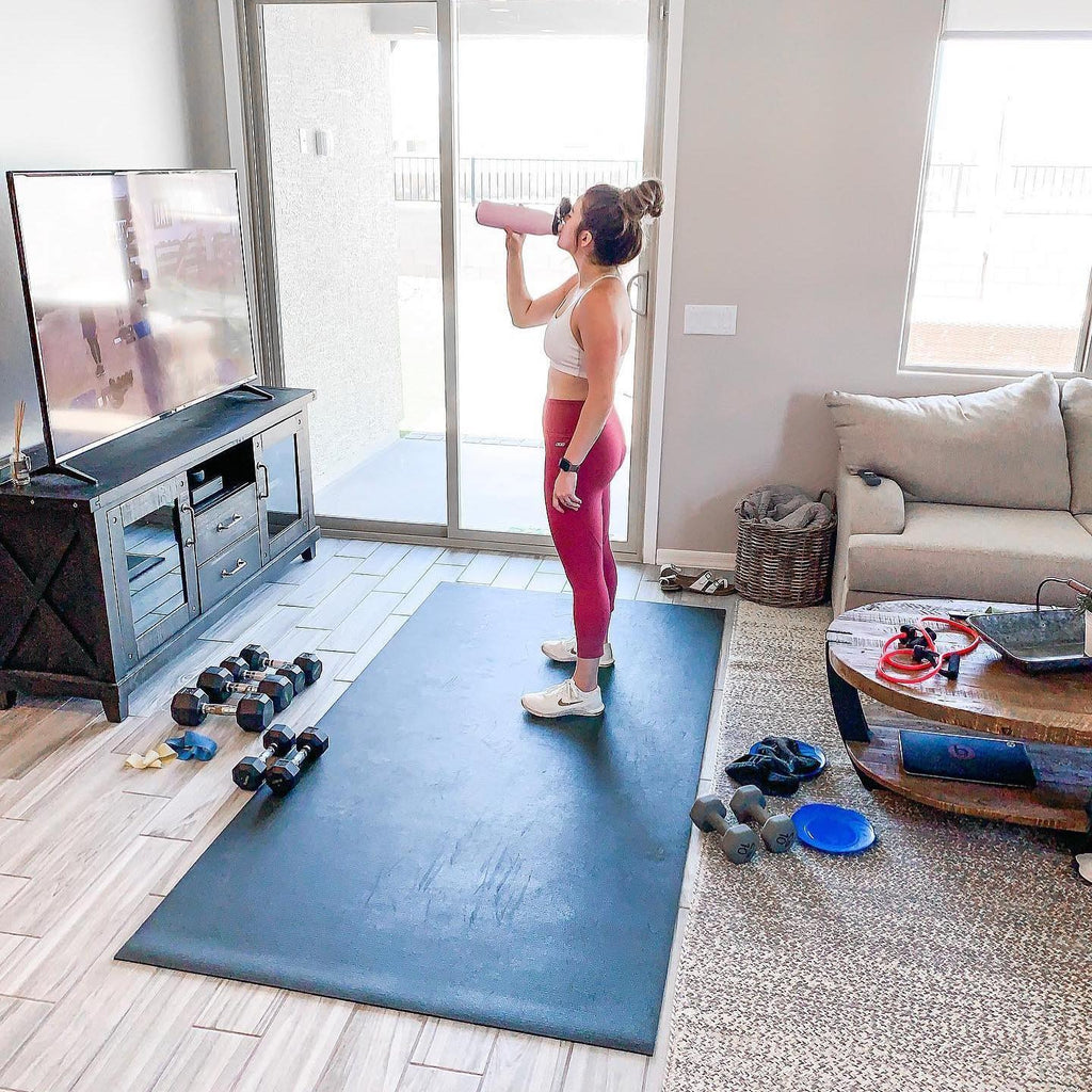 Woman taking a water break on a large black exercise mat after a workout