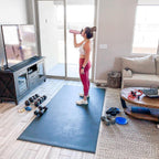 Woman taking a water break on a large black exercise mat after a workout