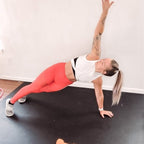 Woman in sneakers holding a side plank with one arm raised on a large black exercise mat