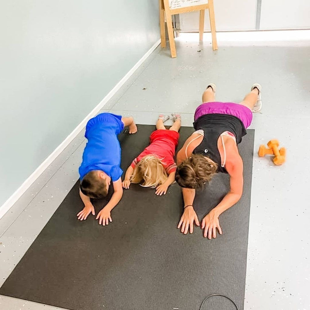 Mom and her kids stretching together on a large black yoga mat