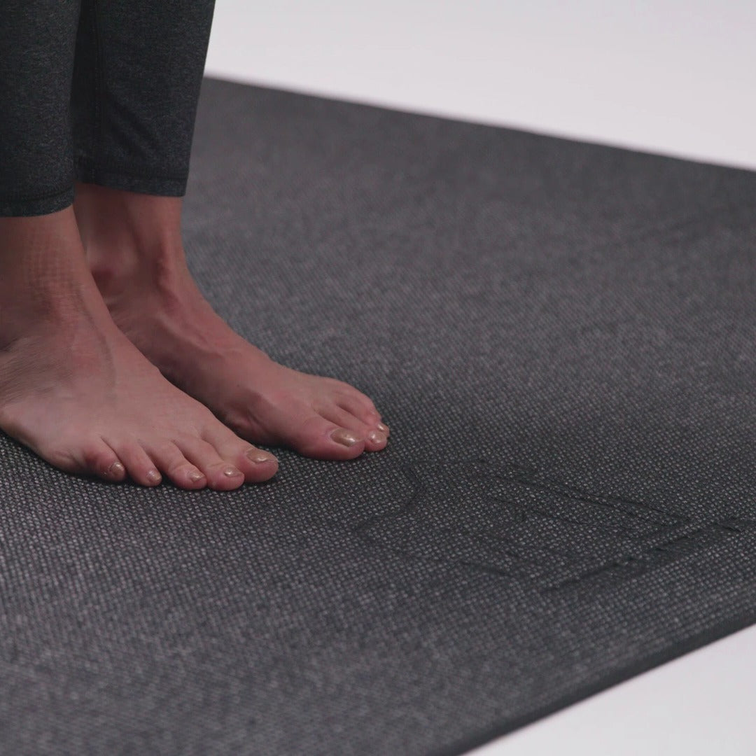 Bare feet standing on a large black yoga mat with the gorilla logo