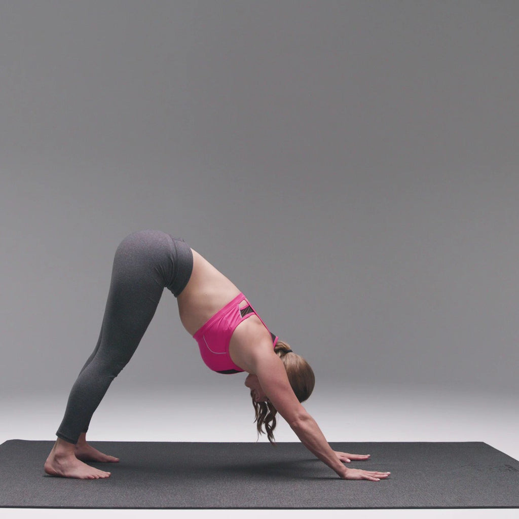 Woman in downward dog on a large black yoga mat