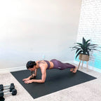 Barefoot woman holding a forearm plank on a large black yoga mat