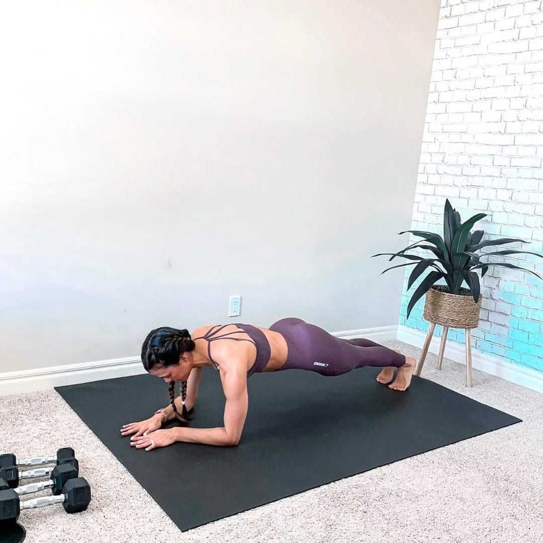Barefoot woman holding a forearm plank on a large black yoga mat
