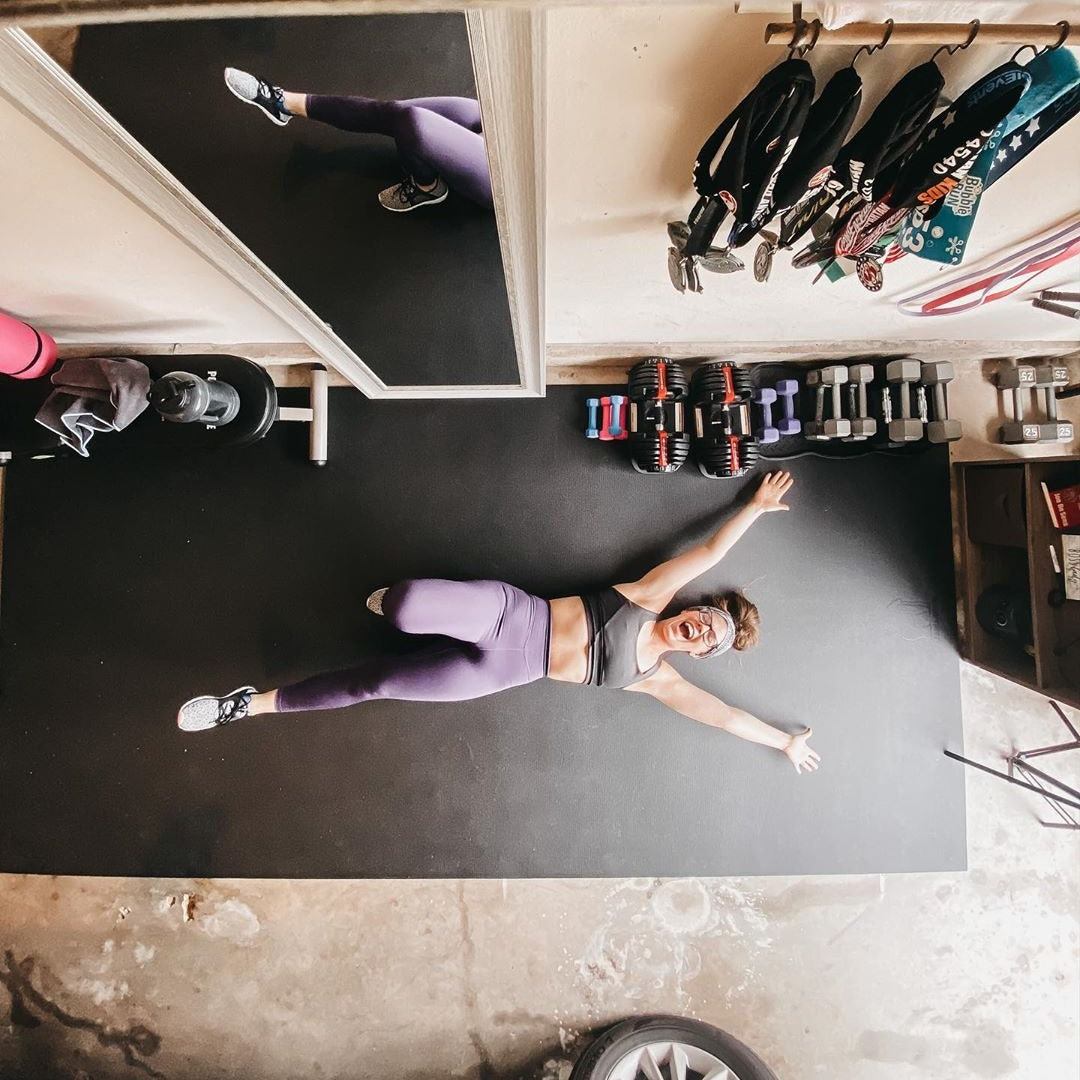 Overhead view of a woman stretched out on a large black exercise mat in her garage gym