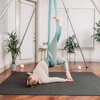 Woman in an aerial yoga bridge over a large black yoga mat