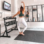 Woman in a barefoot barre plie on a large black mat in her home gym