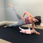 Mom in a side plank beside her baby on a large black yoga mat