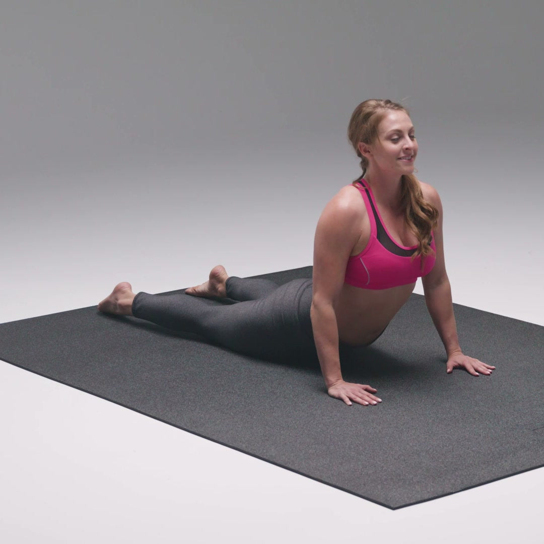 Woman smiling in cobra pose on a large black yoga mat, the whole mat in view