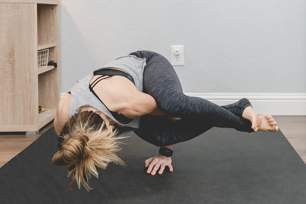 Woman in an arm balance on a large black mat in a bright room
