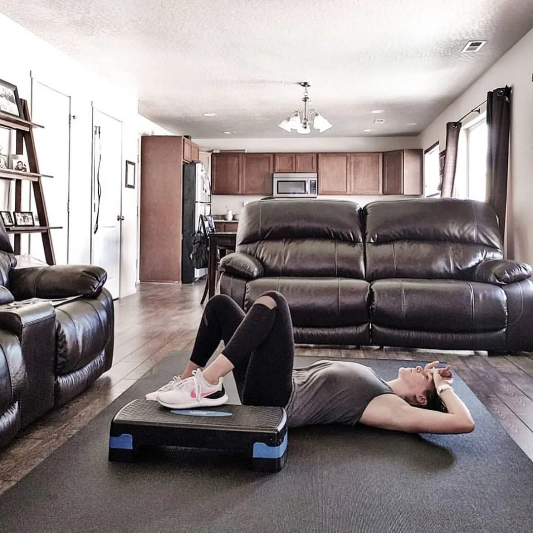 Woman lying on a large mat in her living room, sneakers up on a step platform, leather sofas behind