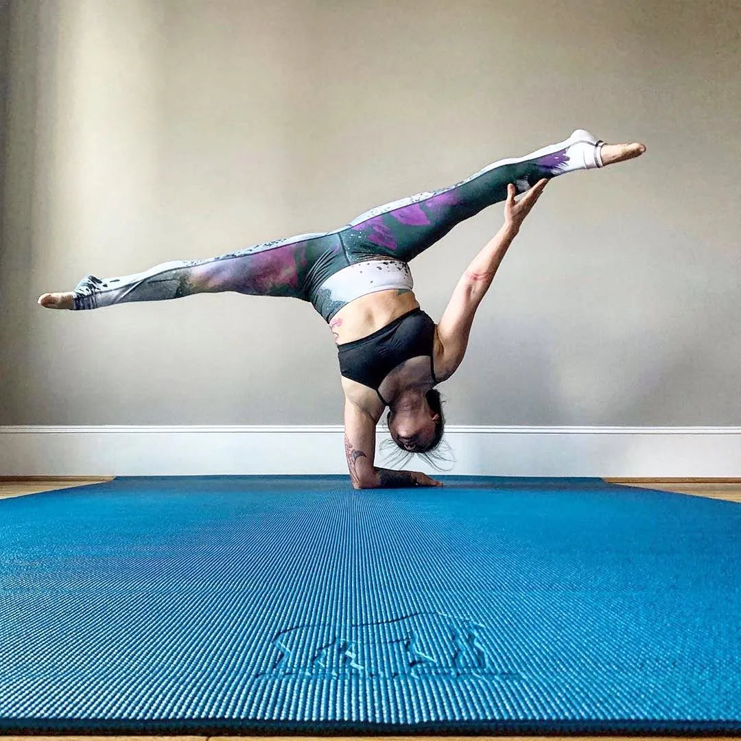 Woman in an inverted split balance on a large teal yoga mat