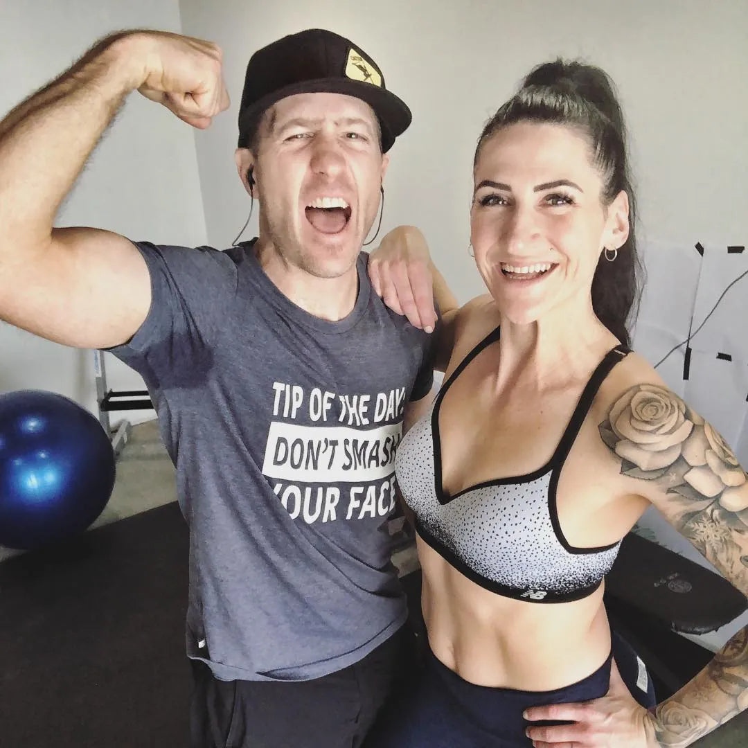Couple smiling and flexing after a workout, a large black mat behind them