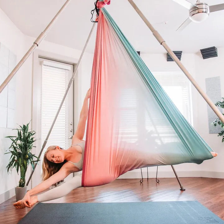 Woman in an aerial yoga silk above a large mat