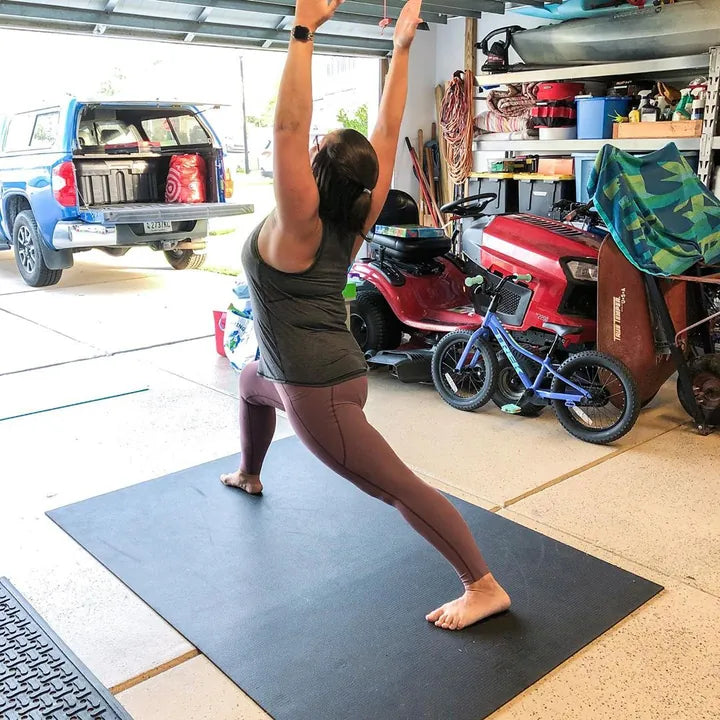 Woman in a standing stretch on a black mat in a garage next to a truck and bikes