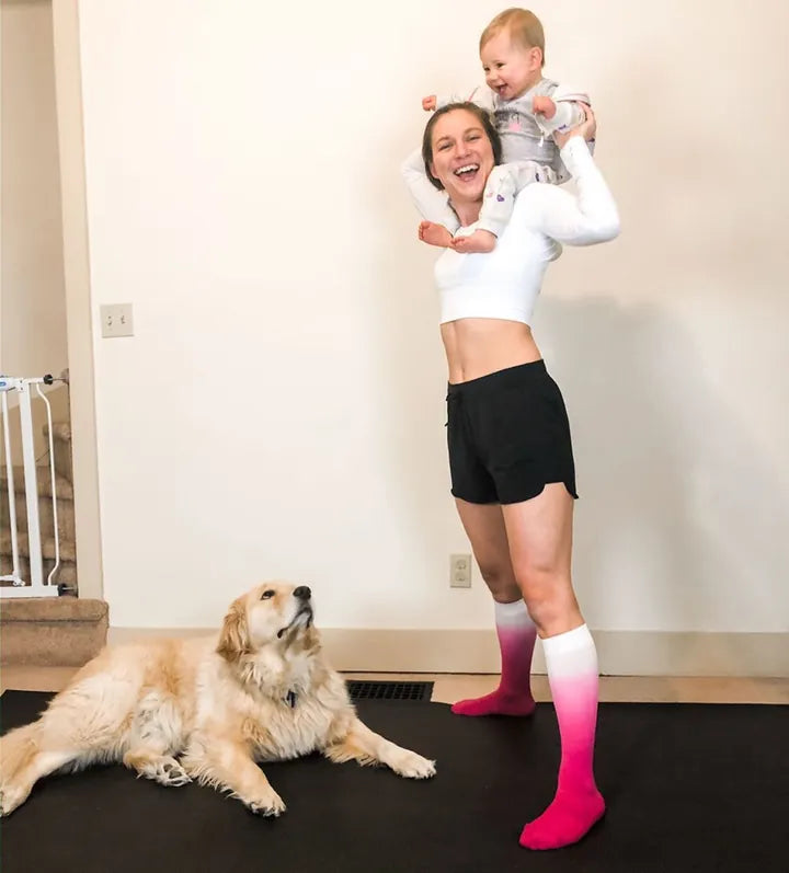 Mom holding her baby on her shoulders on a black mat, golden retriever lying beside her