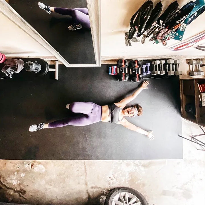 Overhead view of a woman stretched out on a large black exercise mat in her garage gym