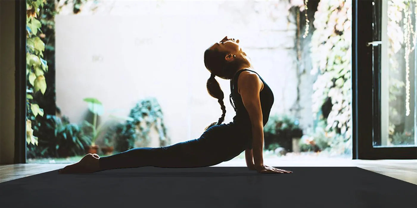 Woman in cobra pose on a large black mat, silhouetted against a bright open doorway